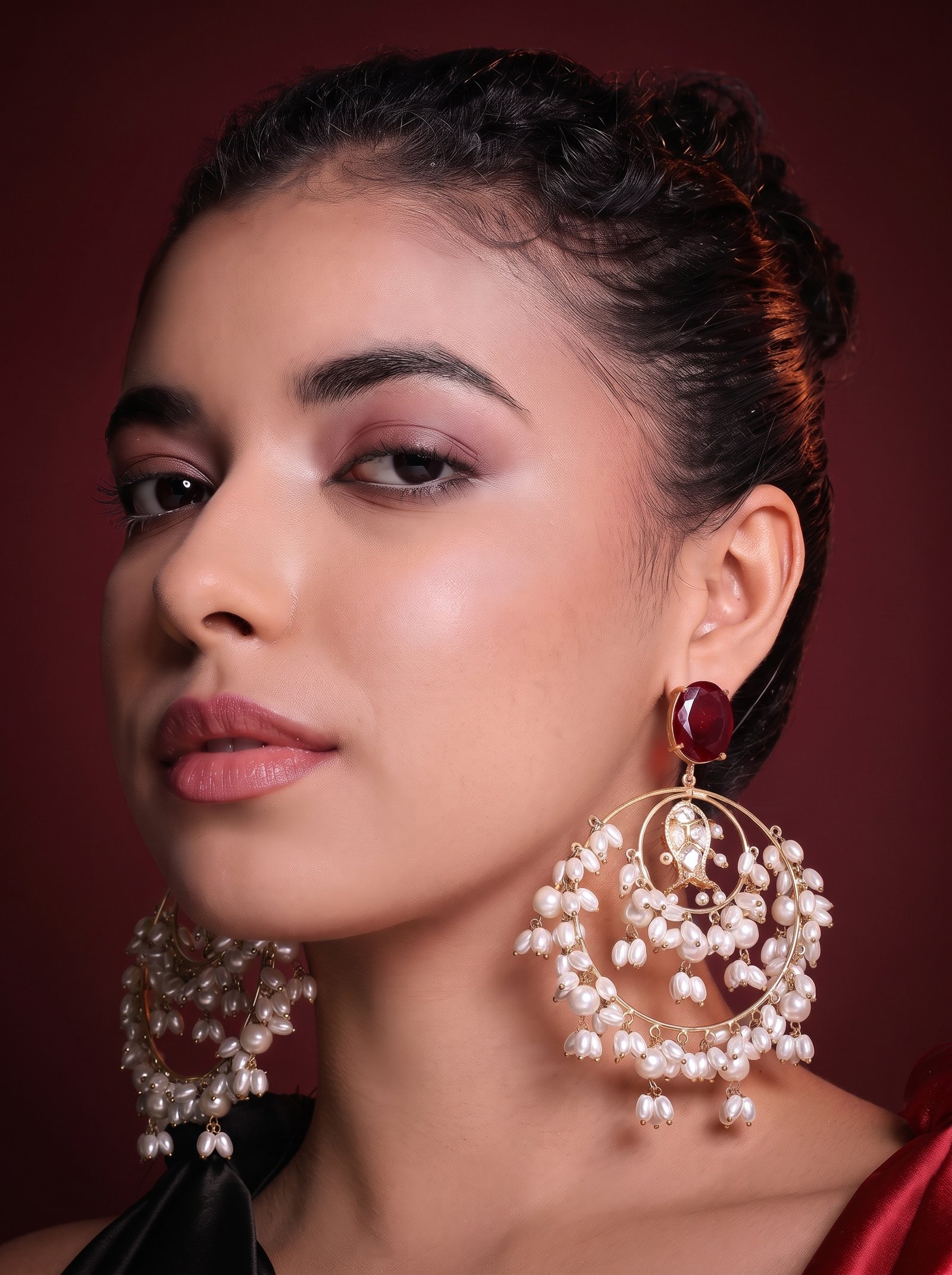A woman wearing Le Agapi pearl-cascade hoop earrings with a red onyx stud