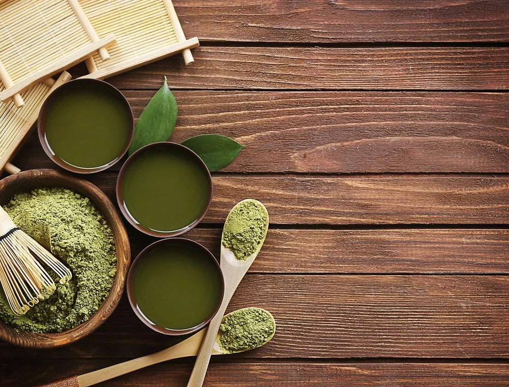 Matcha powder, bamboo whisks, and green tea cups arranged on a wooden table