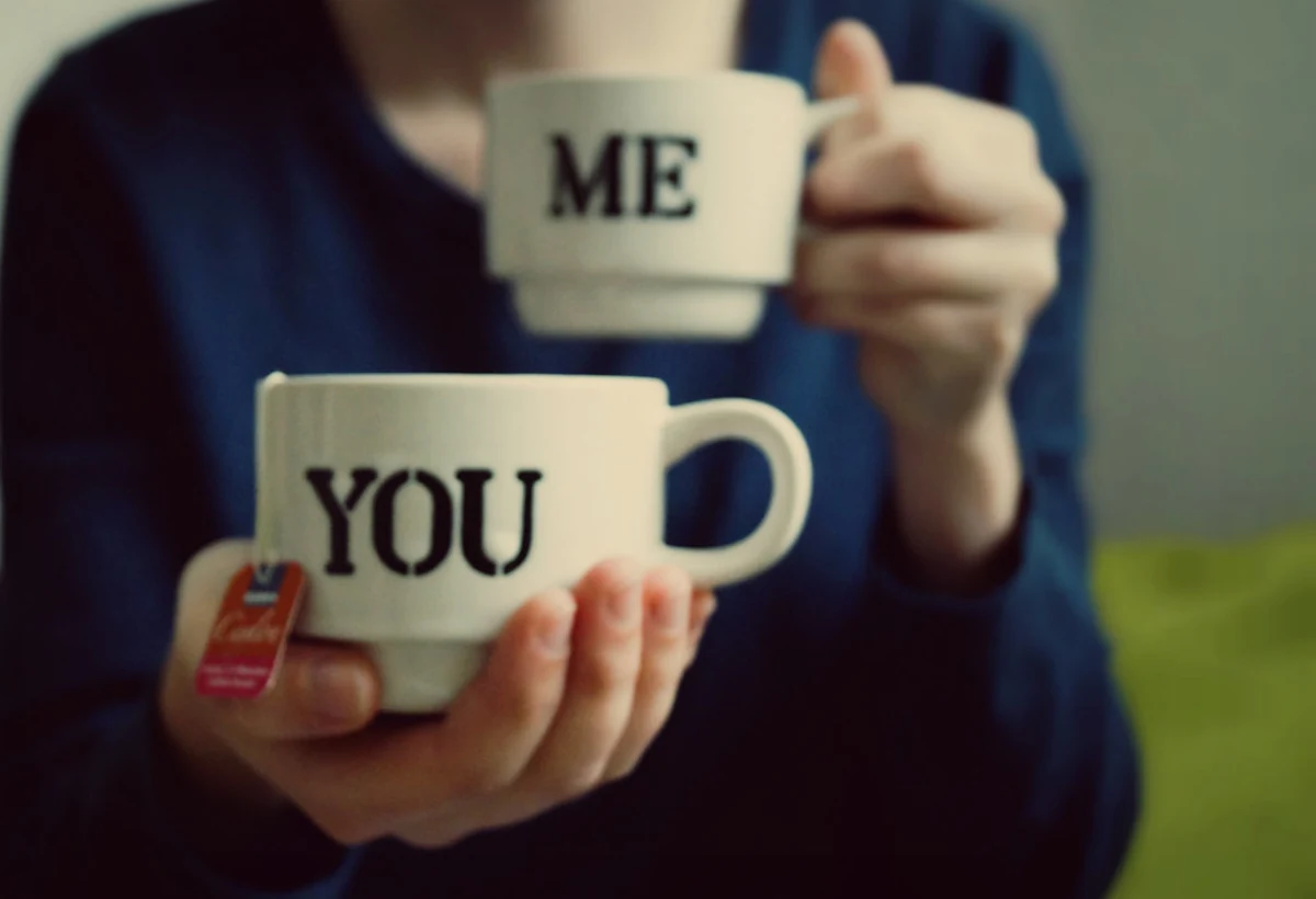 Two people sharing tea from cups marked you and me