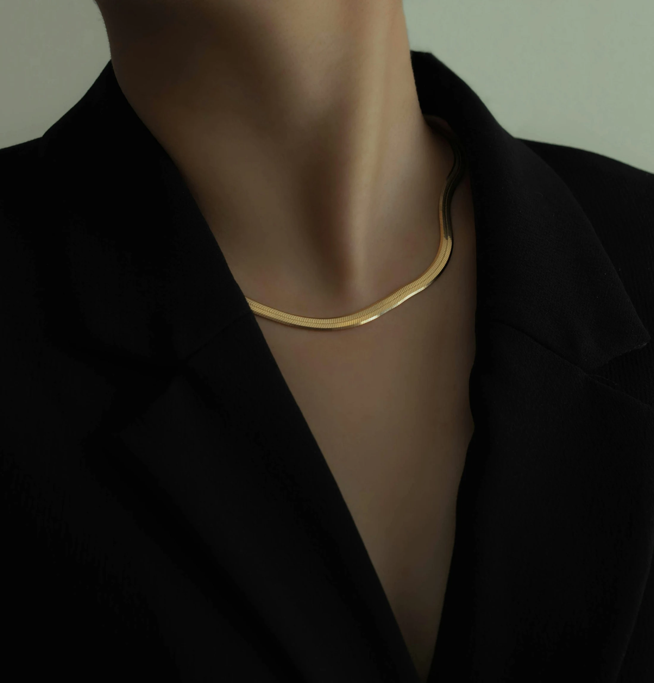 Close view of a polished gold line necklace worn with a black tailored jacket