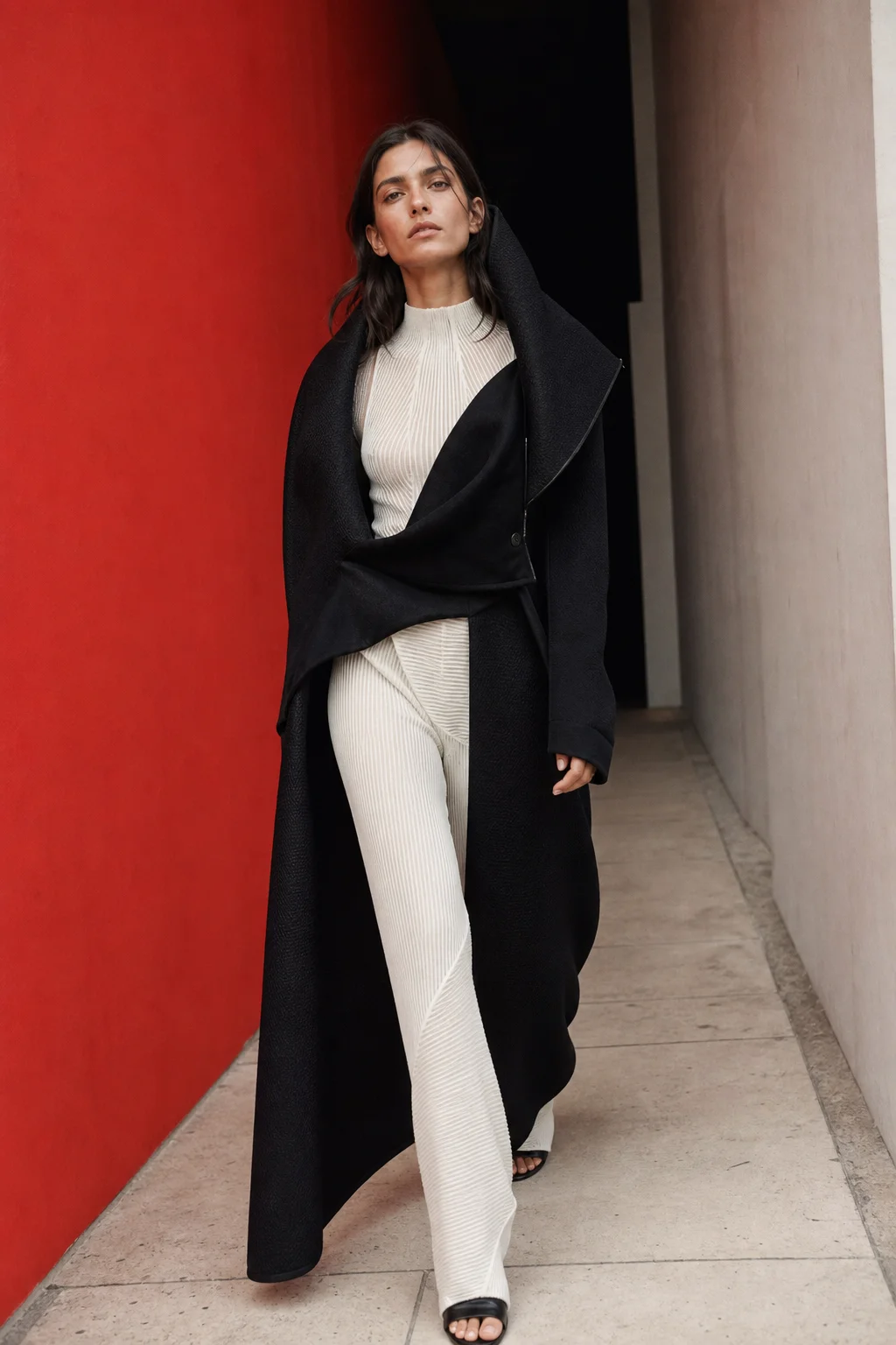Model in sculptural black and white clothing walking through a red concrete corridor
