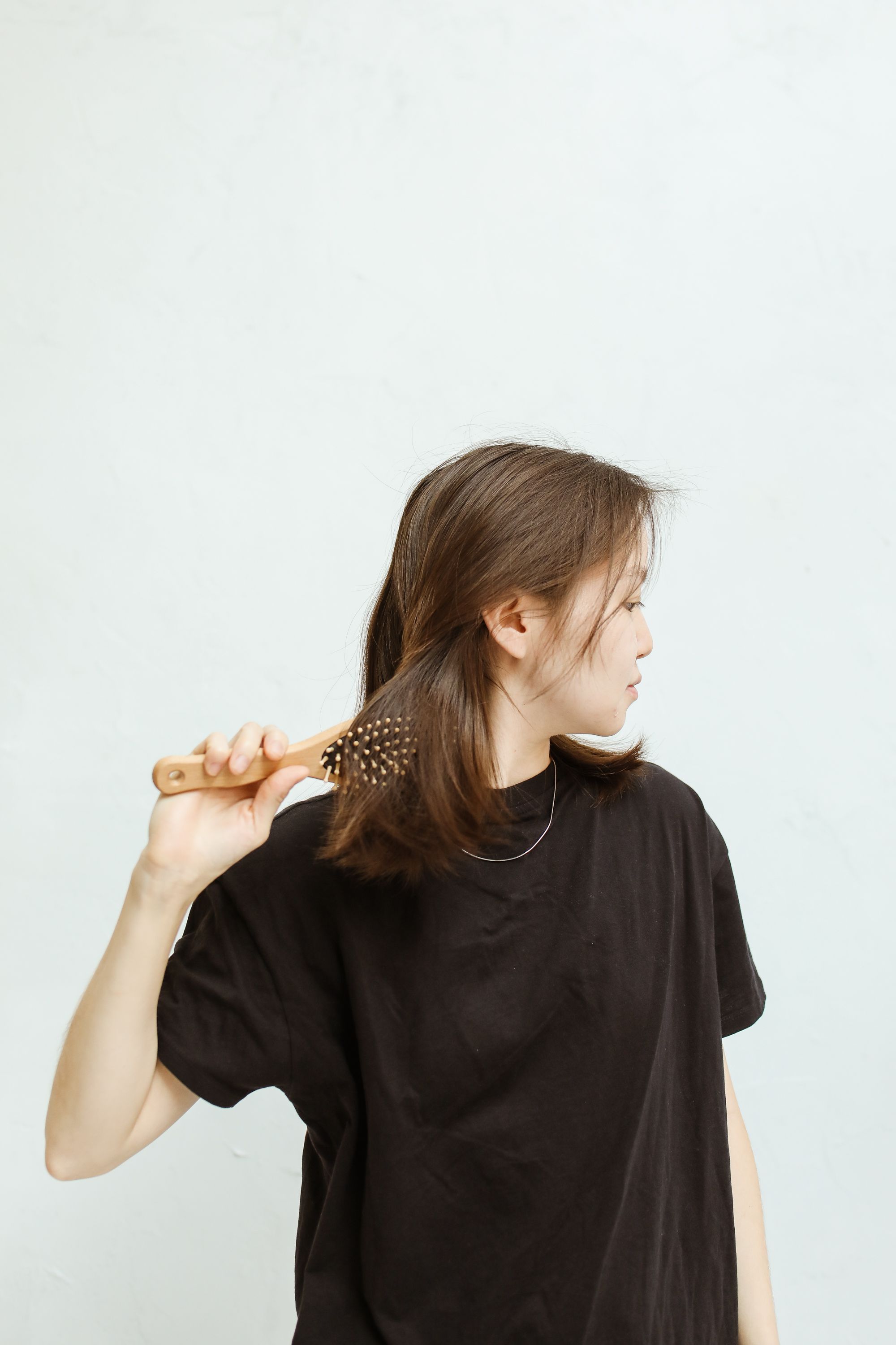 Woman gently combing her hair with a wooden brush against a soft neutral background